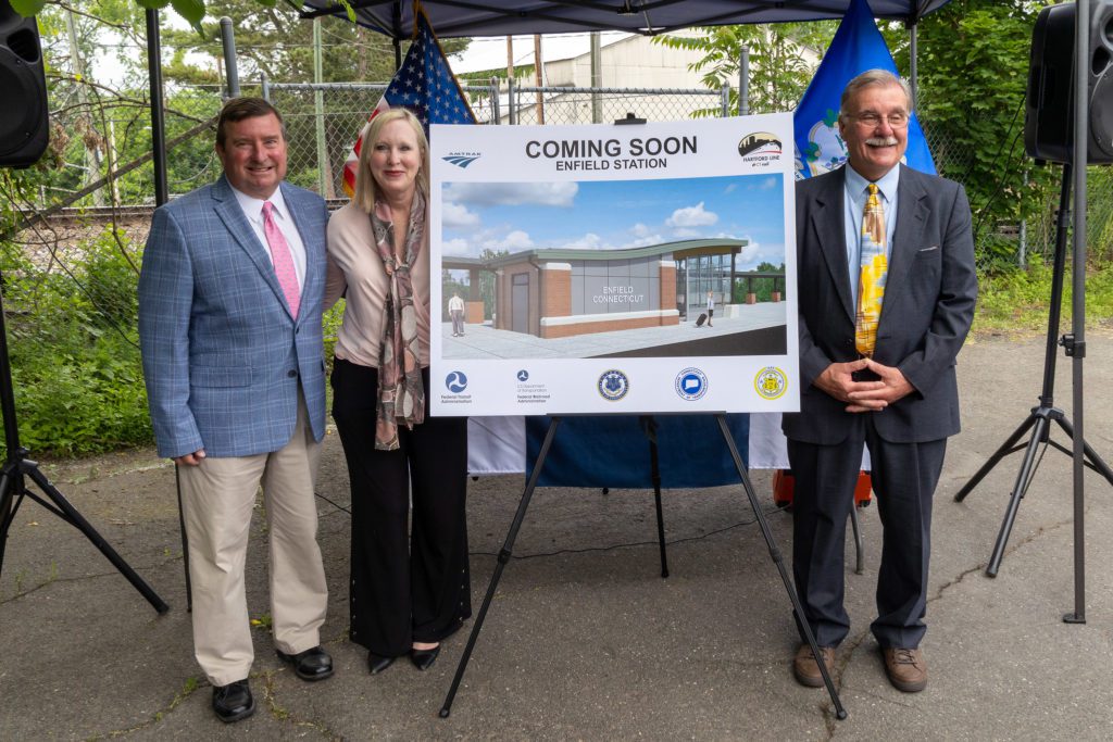 Sen. Kissel, Rep. Hall and Rep. Arnone stand next to a rendering showing the Enfield Train Station